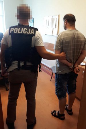policjant trzyma zatrzymanego skutego kajdankami założonymi na ręce trzymane z tyłu