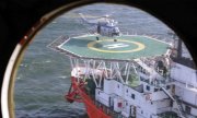 Lądowanie na helipadzie płynącego statku widziane przez okrągły wizjer z góry.