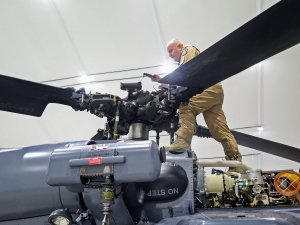 Policyjny mechanik lotniczy dokonuje przeglądu przed lotem mocowania łopat śmigłowca S70i Black Hawk.