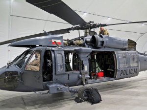 Śmigłowiec S70i Black Hawk w hangarze, podczas przeglądu technicznego wykonywanego przez dwóch mechaników.