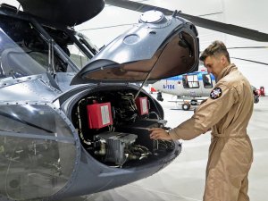 Policyjny mechanik lotniczy dokonuje przeglądu instalacji umieszczonej w przedniej części kadłuba śmigłowca S70i Black Hawk.