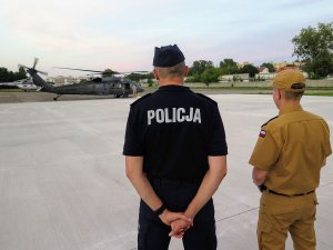 zastępca komendanta głownego policji stoi odwrócony plecami z policyjnym lotnikiem, obaj patrzą na policyjnego Black Hawka