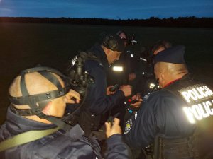 ćwiczenia, widok nocny: pięciu umundurowanych policjantów stoi w terenie w grupce i sprawdzają trzymany w rękach sprzęt.