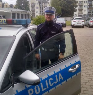 umundurowany policjant stoi przed radiowozem