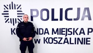 umundurowany policjant stoi przy napisie: Policja, Komenda Miejska Policji w Koszalinie
