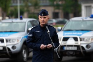 Komendant Główny Policji przemawia do policjantów wyjeżdżających na Litwę na tle policyjnych pojazdów