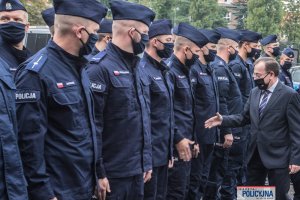 Minister SWiA wyciąga dłoń do umundurowanych policjantów stojących w dwuszeregu