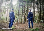 Na zdjęciu jest dwóch umundurowanych policjantów stojących tyłem w lesie.