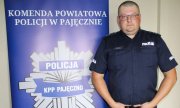 Umundurowany policjant stoi na tle baneru z napisem Komenda Powiatowa Policji w Pajęcznie