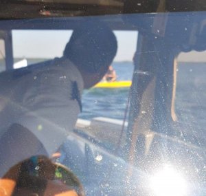 Policjant w łodzi służbowej podpływa do przewróconej żaglówki