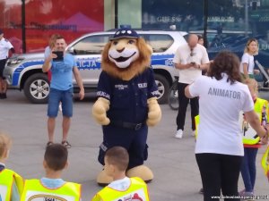Pod centrum handlowym dzieci wspólnie z komisarzem lwem i policjantkami i animatorem tańczą i śpiewają.