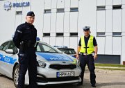 Dwóch policjantów stoi przy radiowozie, w tle budynek Komendy Miejskiej Policji w Suwałkach