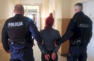 Dwóch policjantów prowadzi zatrzymaną kobietę w kajdankach