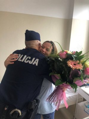 Kobieta z bukietem kwiatów ściska w podziękowaniu policjanta