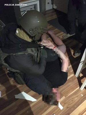 zatrzymany leży na podłodze a policyjny  antyterrorysta zakłada mu kajdanki