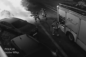 Zapis z kamer zaparkowanych aut w tym jedno palące się, obok wóz strażacki i strażacy próbujący ugasić pożar