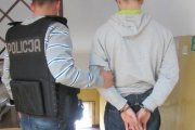 policjant w kamizelce z napisem Policja na plecach prowadzi zatrzymanego