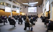 Europejska Konwencja Szefów Policji (EPCC)  państw Unii Europejskiej w Hadze- zebrani siedzą na krzesłach w sali z zachowaniem dystansu i w maseczkach na twarzach - widok z tyłu a przed nimi i po bokach widać telebimy na których widnieje przemawiający mężczyzna
