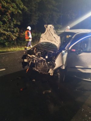 Zniszczona przednia cześć jasnego samochodu Daewoo Matiz. W głębi widoczny strażak