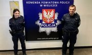 policjant i policjantka, którzy odnaleźli chłopca w tle na ścianie napis komenda powiatowa policji w Wieliczce i jej herb