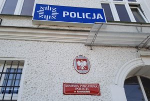 Biały budynek z logo Policji i tablicą informacyjną
