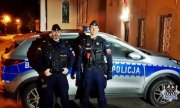 Wieczór. dwaj umundurowani policjanci stoją przed radiowozem