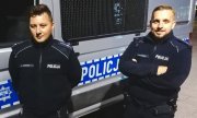 dwaj policjanci stoją przed radiowozem policyjnym