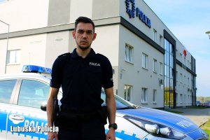 Umundurowany policjant stoi przed budynkiem Komendy Powiatowej Policji w Międzyrzeczu, za nim widoczny radiowóz