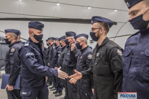 wnętrze hangaru, Komendant Główny Policji gratuluje policyjnym lotnikom stojącym w szeregu