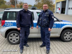 dwaj umundurowani policjanci przy radiowozie