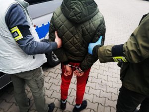 Zatrzymany obywatel Rumunii. Ma założone kajdanki z tyłu. Trzymają go policjanci kryminalni