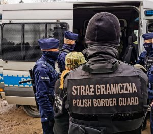 dwoje funkcjonariuszy straży granicznej i czterech policjantów stoi przed otwartym radiowozem - widok z tyłu