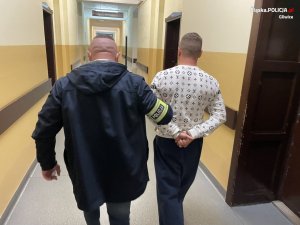 Policjant prowadzi korytarzem skutego kajdankami mężczyznę