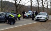 trzy radiowozy stojące na drodze i grupa policjantów w trakcie zatrzymywania mężczyzny