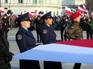 Policjantki Kompanii Reprezentacyjnej Policji niosą flagę polską wraz z przedstawicielami innych służb mundurowych