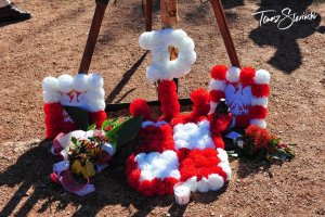 białe i czerwone kwiaty ułożone w kształt znaku Polski Walczącej, po bokach godła polski obramowane białymi i czerwonymi kwiatami