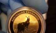 dłoń w niebieskiej rękawiczce trzyma złotą okrągłą monetę z wizerunkiem kangura