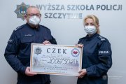 policjant i policjantka w maseczkach ochronnych trzymają symboliczny czek, na którym wpisana jest kwota 20067 złotych 50 groszy zebranych pieniędzy