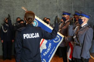 dwoje policjantów składa ślubowanie stojąc z prawą ręka uniesiona do góry przed opuszczonym sztandarem, trzymanym przez poczet sztandarowy