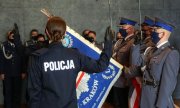 dwoje policjantów składa ślubowanie stojąc z prawą ręka uniesiona do góry przed opuszczonym sztandarem, trzymanym przez poczet sztandarowy