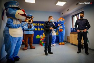policjanci stoją z maskotkami podczas pogadanki z przedszkolakami