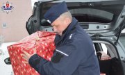 policjant trzyma paczkę z prezentami, za nim widać w otwartym bagażniku samochodu inne paczki