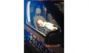 Zdjęcia zrobione na zewnątrz - ukazuje wnętrze radiowozu, w którym siedzi policjant, a na ramieniu trzyma śpiącego niemowlaka