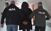 policjanci w kurtkach z napisem Policja na plecach prowadzą zatrzymanego - widok z tyłu
