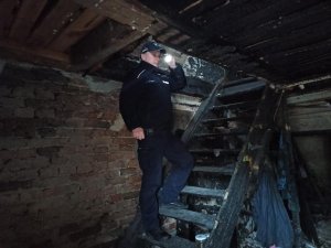 Policjant stoi na schodach i świeci latarką, w budynku gdzie przebywał bezdomny