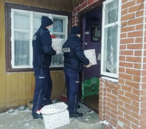 Umundurowani policjanci trzymają świąteczne paczki i stoją przed wejściem do domu