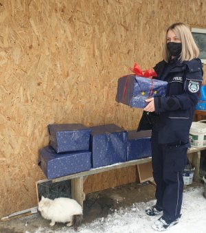 Umundurowana policjantka trzyma w rękach świąteczną paczkę, obok na ławce stoją poukładane inne paczki