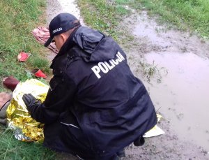 policjant podczas interwencji ratowania wychłodzonego mężczyzny. Policjant schylony okrywa mężczyznę srebrno-złotą folią