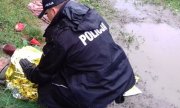 policjant podczas interwencji ratowania wychłodzonego mężczyzny. Policjant schylony okrywa mężczyznę srebrno-złotą folią
