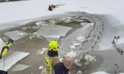 akcja ratunkowa na rzece, policjant na desce ortopedycznej na lodzie trzyma psa i jest ciągnięty za linkę przez druha strażaka  i innego policjanta